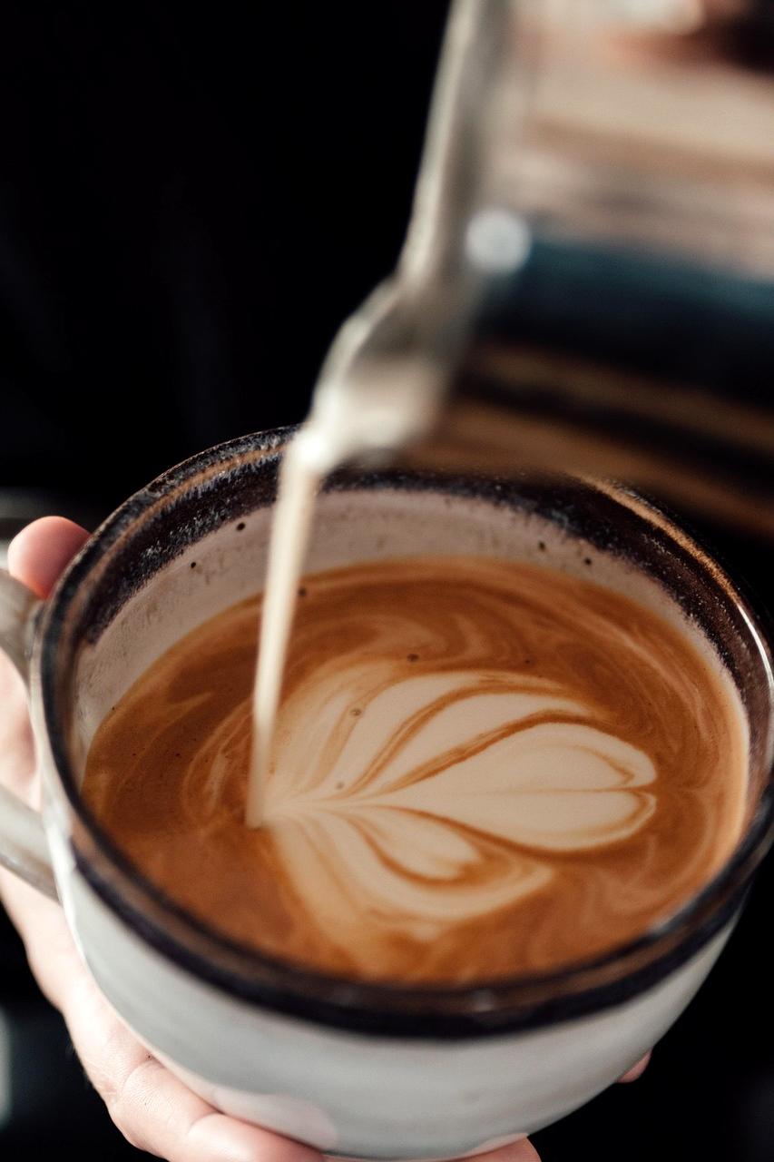 Barista che versa latte caldo per cappuccino con decorazione a cuore